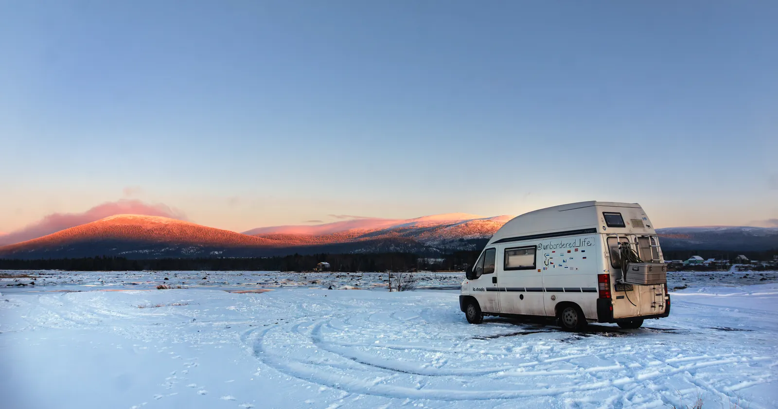 Van im verschneiten Feld bei Sonnenuntergang